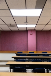 A classroom that has the lights on. There is a purple wall and the room has chairs and desks.