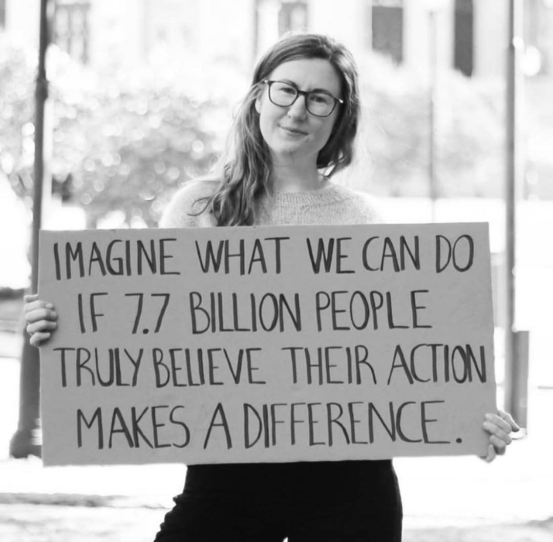 woman holding cardboard sign that says imagine what we can do if 7 billion people believe our actions make a difference