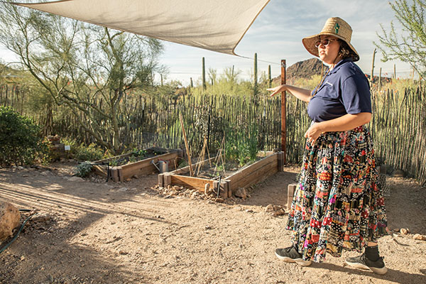 A woman stands in front of raised garden beds pointing out garden features