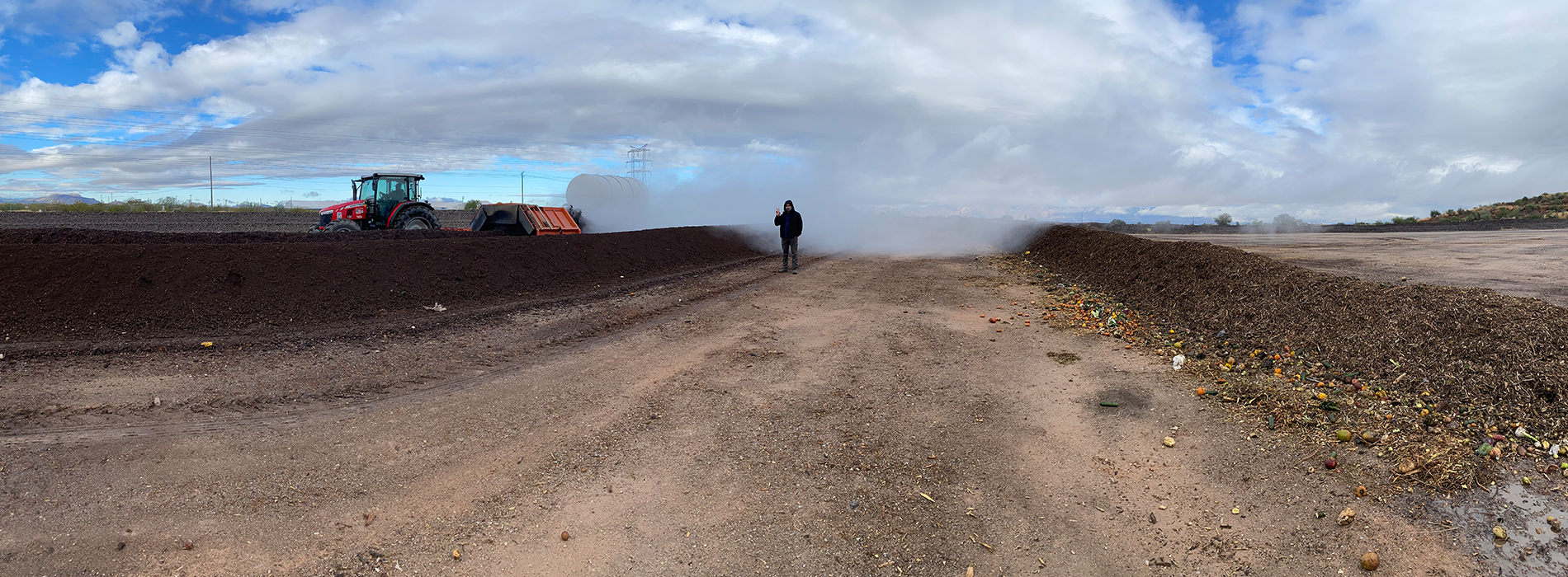 Student standing on a cleared path along a compost field