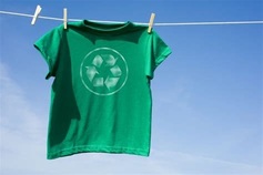 Green tshirt with recycle symbol hanging on clothesline, with a backdrop of blue sky.