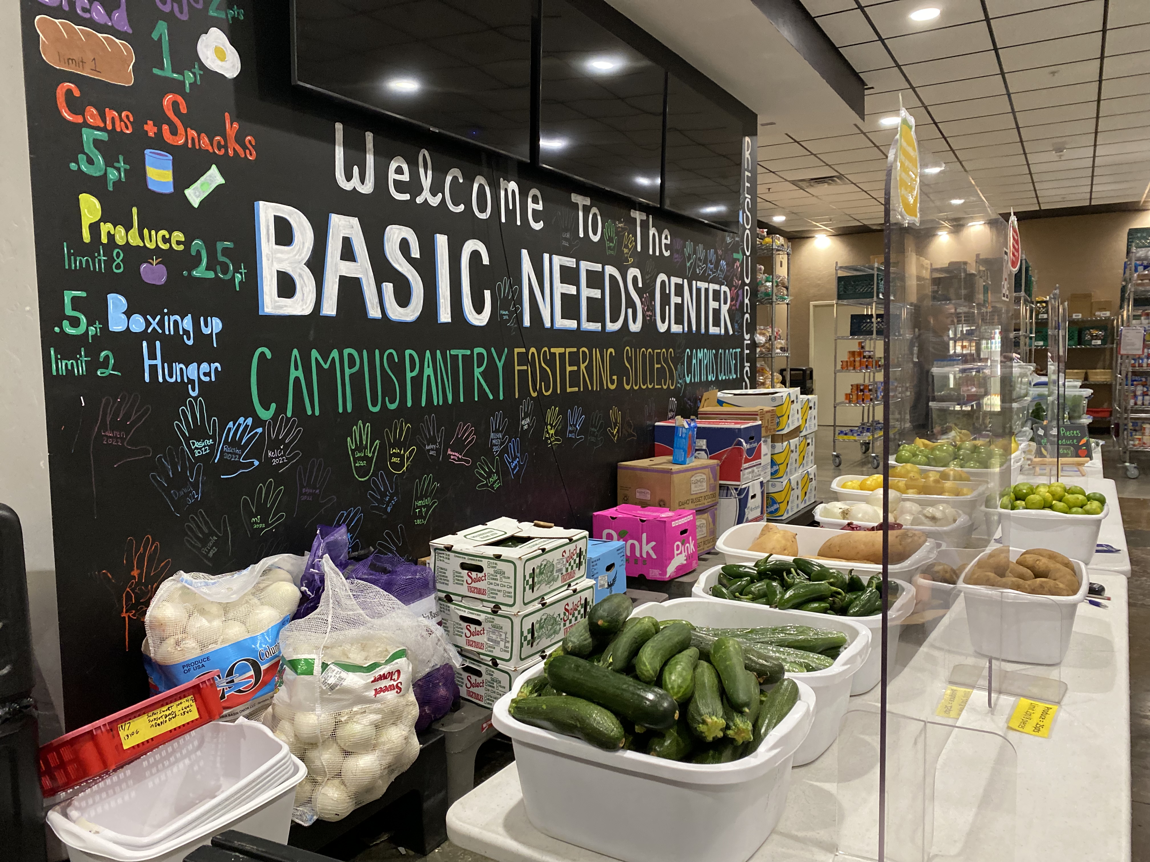 A table full of produce and boxes in front of a large black chalkboard wall.