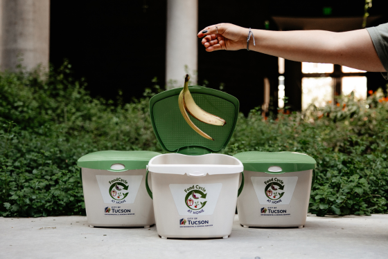 Hand dropping a banana peel into an open FoodCycle at Home food waste pail. 