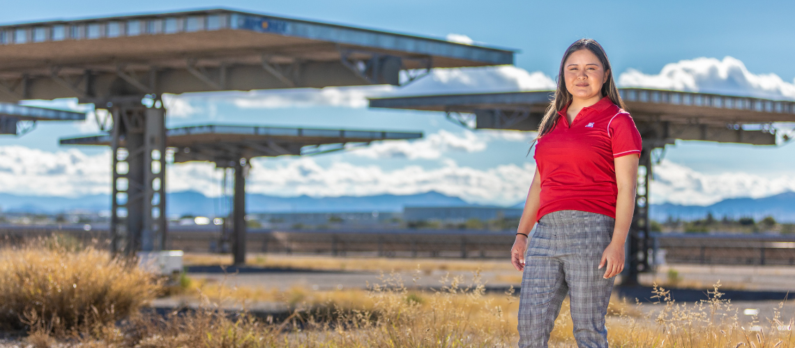 a female student stands in a grassy field with large solar panel installations in the background