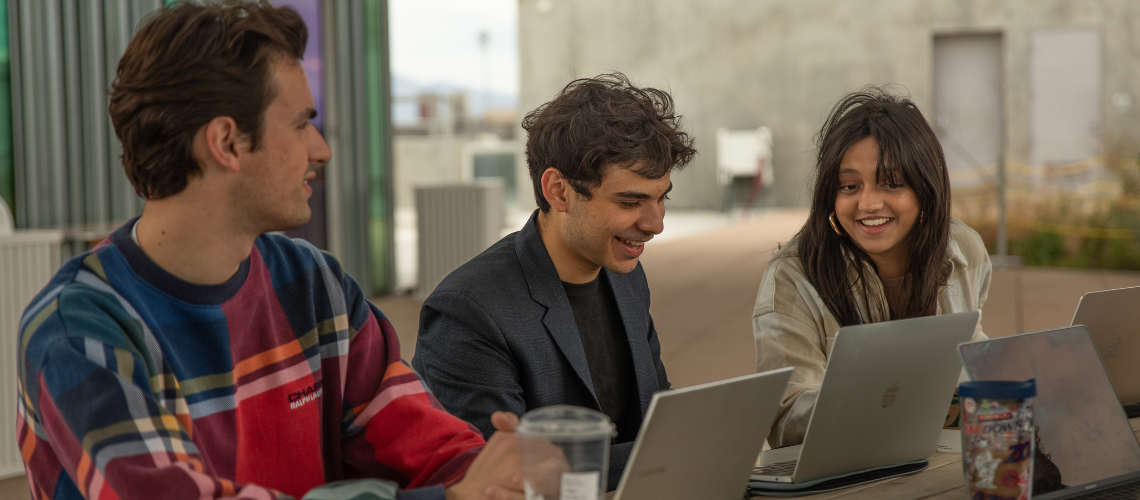 3 campus sustainability fund committee members sit together at a table with their laptop computers open as the smile at eachother