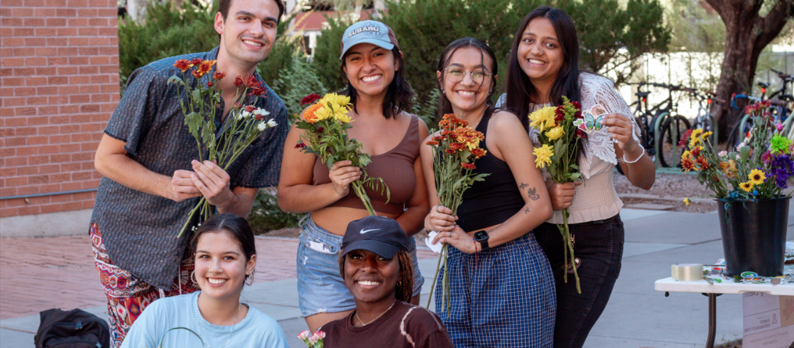 Five students pose together, each holding a bouquet of flowers