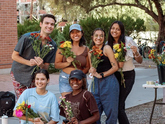 A group of people smiling and holding various types of flowers.