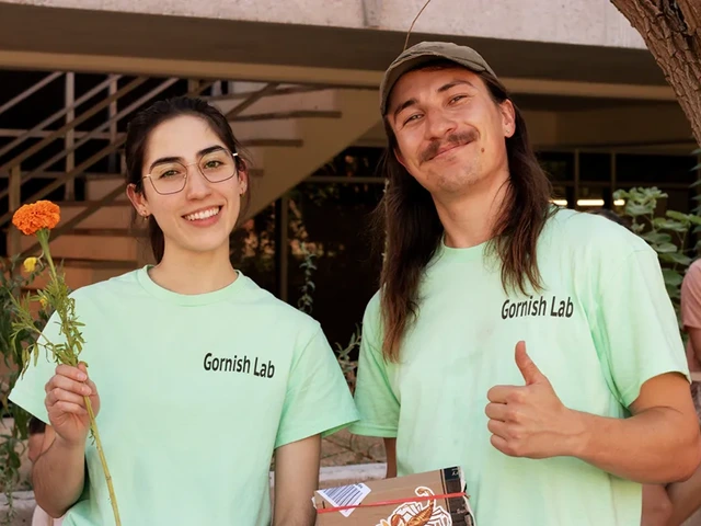 Two people smiling. One is holding a orange flower and the other is holding a thumbs up.