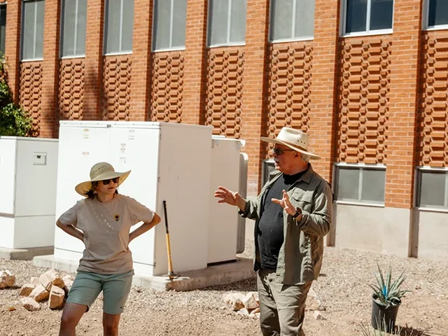 Two people standing in front of a building, talking to each other.
