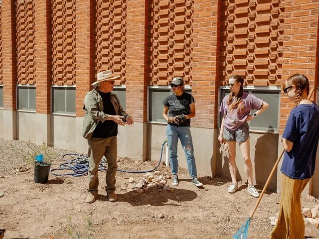 Four people standing around each other listening to one person talk. Some people are holding shovels or work gloves.