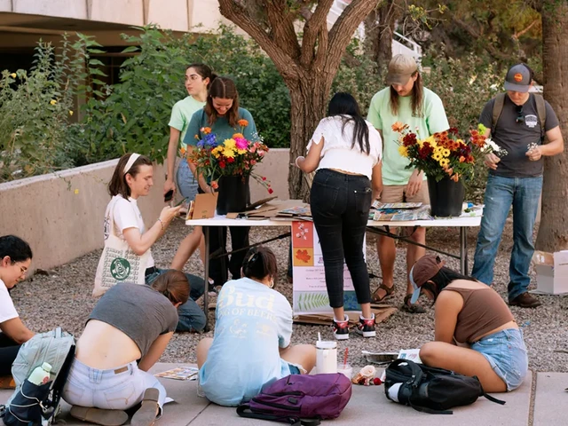 A group of people sitting in front of a table, pressing flowers using cardboard and newspaper.
