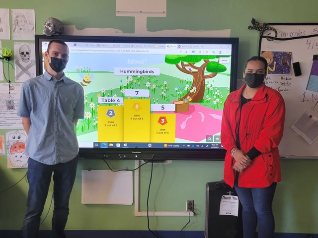 Two classroom educators pose in front of their lesson board. 