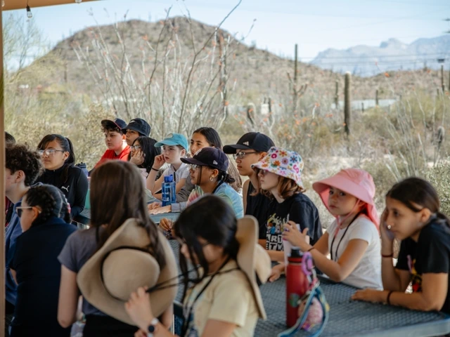 a group of students are seated at outside tables under a ramada during an orientation meeting at Camp Cooper