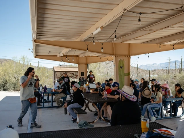 a group of students are seated at outside tables under a ramada during an orientation meeting at Camp Cooper