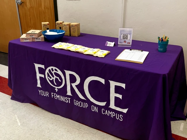 A table covered in a purple cloth with the FORCE logo. On top of the table are various boxes of menstrual cups and wipes. 