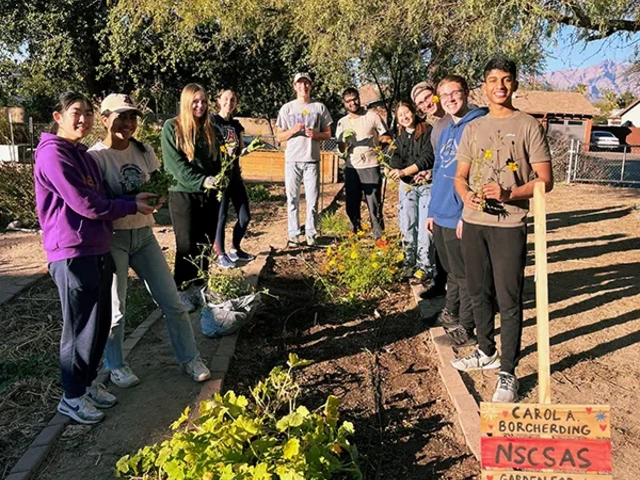 A group of people posing for a photo next to a garden plot.
