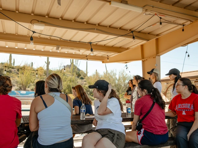 A group of people sitting down underneath a ramada. 