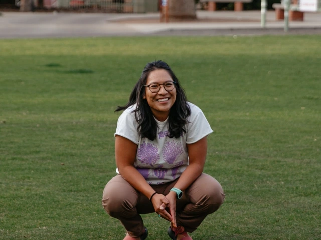 A person squatting down in a grass field talking to a group of people.