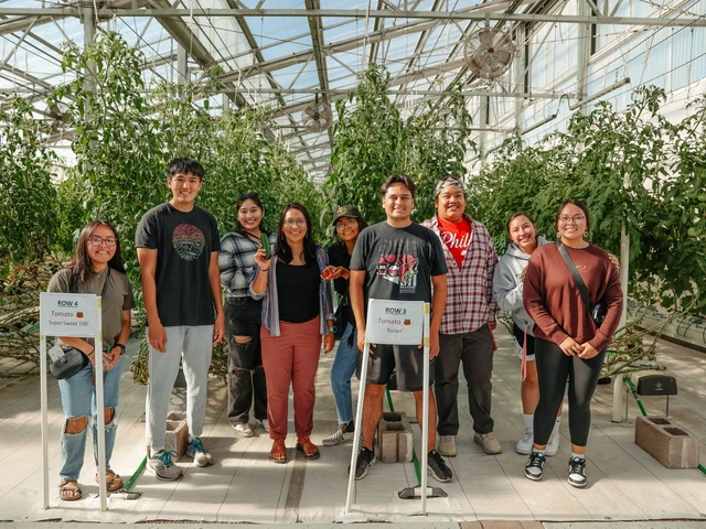 A group of people standing next to each other and smiling for a photo. They are standing in a greenhouse and in front of various types of crops.