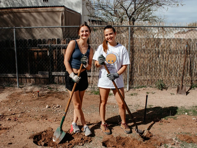 Two people standing next to each other smiling and holding shovels.