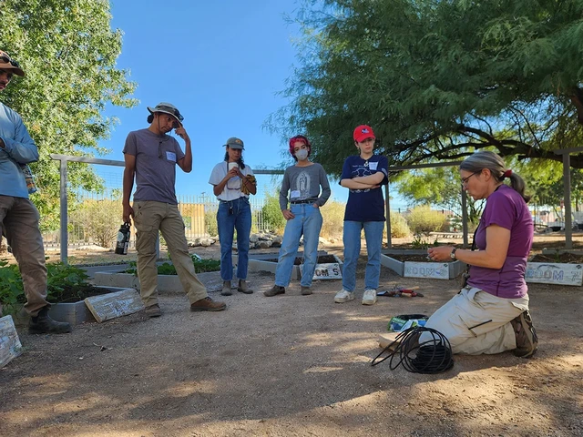A group of people gather around outside to learn from an educator.