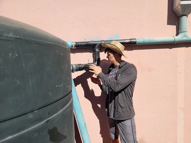 One person is inspecting the pipes that lead to a rainwater cistern.