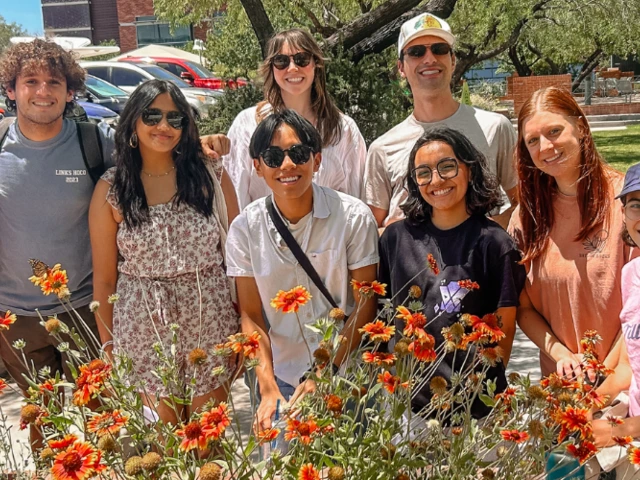 A group of people standing next to each other and smiling behind a flower bush.