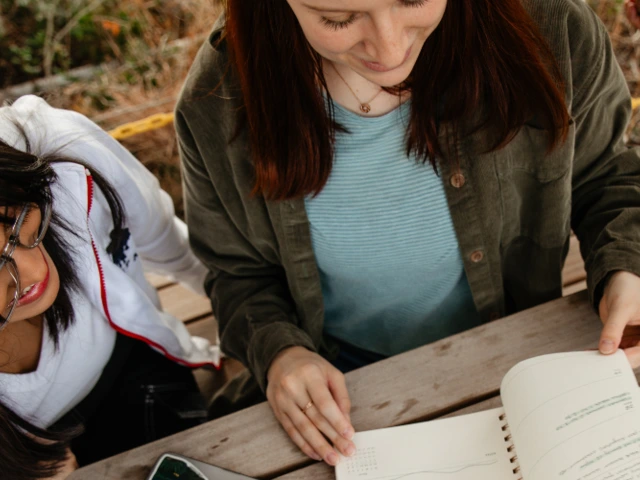 Two women sitting together looking over notes in a notebook