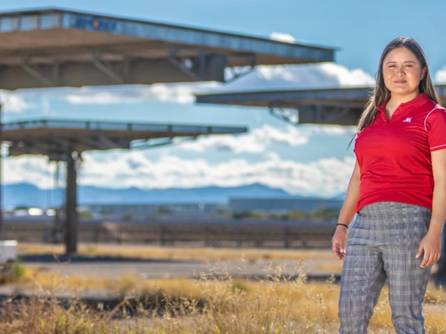a female student stands in a grassy field with large solar panel installations in the background