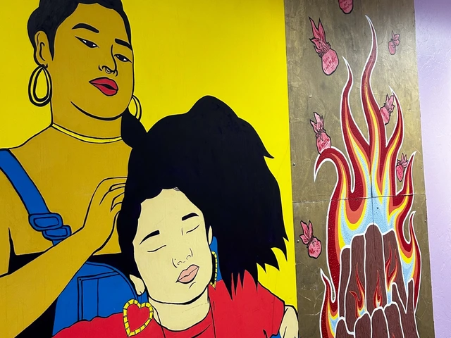 A wall mural where two people are painted. One person is doing the other persons hair. The painting next to them is of wooden logs on fire.
