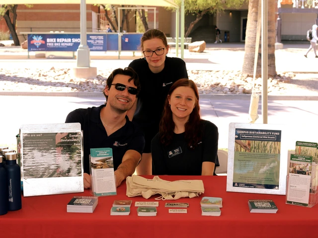Three people posing for a photo behind a table that is covered in outreach material and a red cloth.