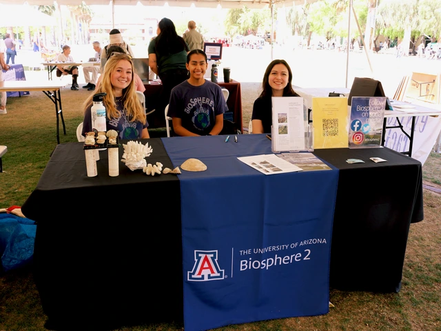 Three people smiling and sitting behind a table covered in outreach material.