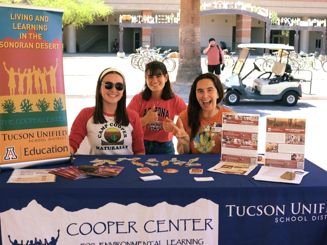 Three people smiling and sitting behind a table covered in outreach material.
