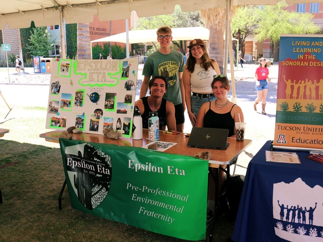 Four people smiling behind a table covered in outreach material.