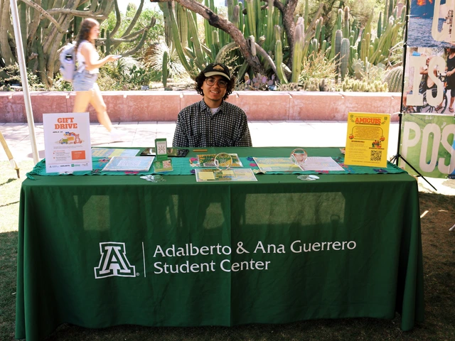 A person smiling and sitting behind a table covered in outreach material.