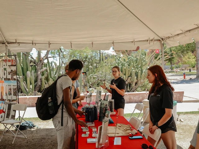 A group of people talking to two other people who are behind a red table.