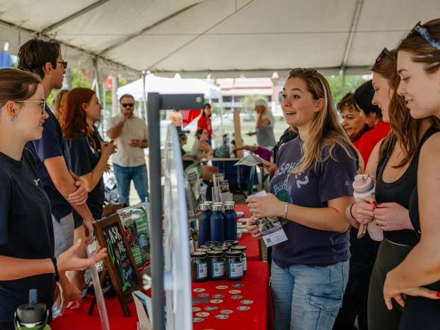 A group of people all talking to one another with a red table in between them. Next to the table is a game wheel that spins.