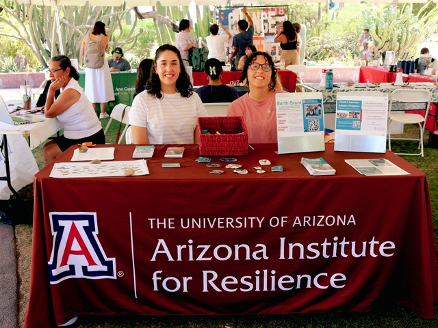 Two people smiling and sitting behind a table covered in outreach material.