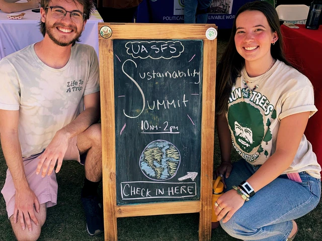 Two people are squatting down next to a chalkboard sign that reads "UA SFS, Sustainability Summit, 10am - 2pm, Check in here".