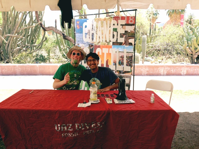 Two people smiling and sitting behind a table covered in outreach material.