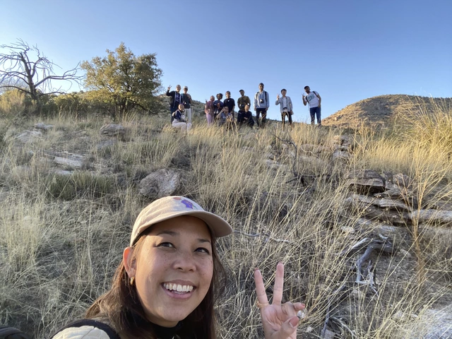 ONe person is taking a selfie with a group of students behind them, standing on a grassy hillside