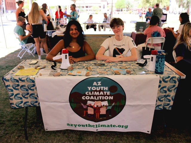 Two people smiling and sitting behind a table covered in outreach material.