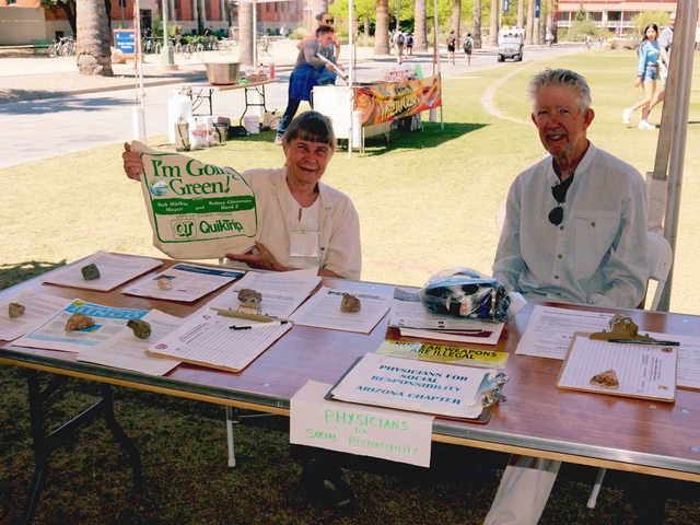 Two people smiling and sitting behind a table covered in outreach material.