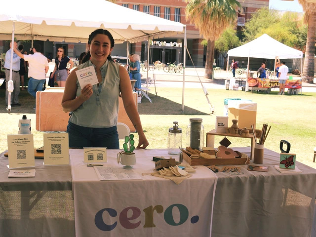 A person smiling and standing behind a table covered in outreach material.