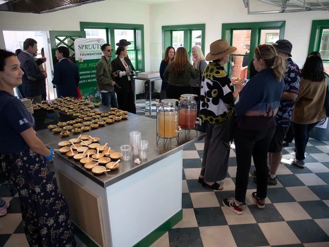 Multiple groups of people converse inside of a house with checkered tiles next to a large counter with rows of food.
