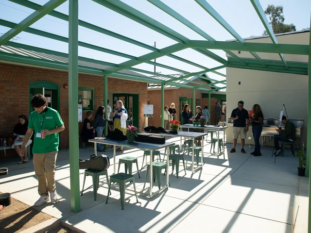 A large green metal structure next to brick houses covers tables, chairs, and people walking underneath it. 