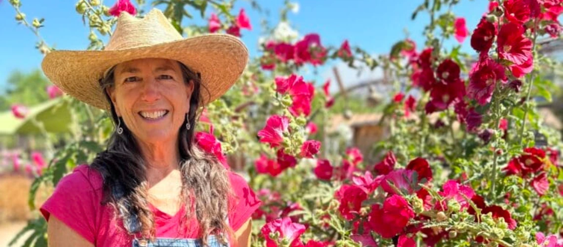 A woman stands in front of several hollihock plants