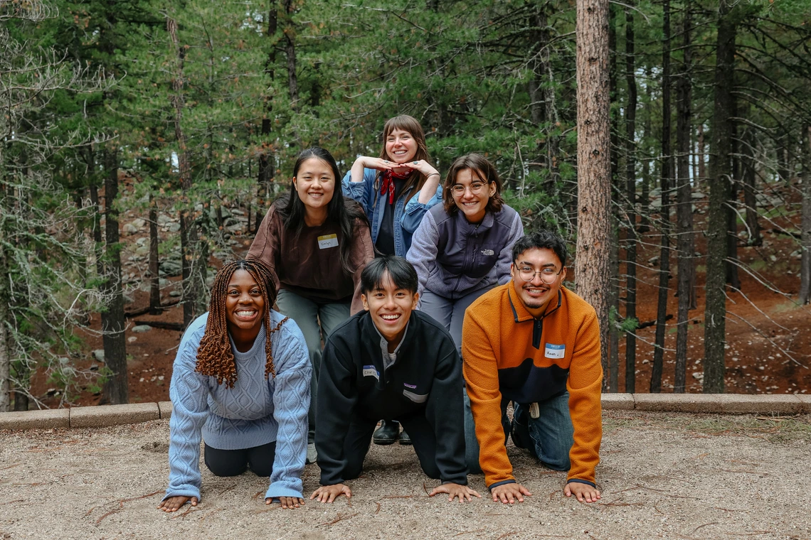 A group of 6 people stacked in a human pyramid in a forest. 