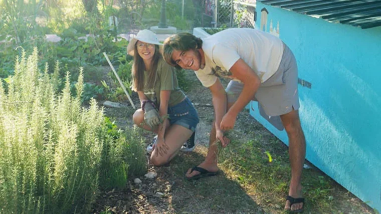 Two smiling gardeners weeding on a sunny day.