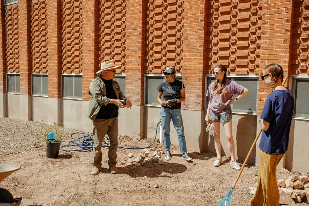 Four people standing around each other listening to one person talk. Some people are holding shovels or work gloves.